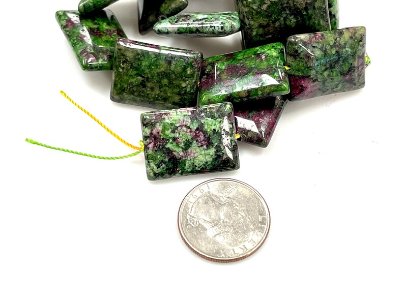 Puede incluir: Cuentas cuadradas con un patr&oacute;n verde y granate, ensartadas en hilo amarillo y verde. Se incluye una moneda como referencia de tama&ntilde;o. Las cuentas miden aproximadamente 1,5 cm cuadrados.