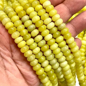 May include: Close-up of strands of yellow-green gemstone beads. The beads are small, round, and have a slightly irregular shape. The color varies from pale yellow to a deeper, olive-green hue. The beads are strung together, forming multiple strands.