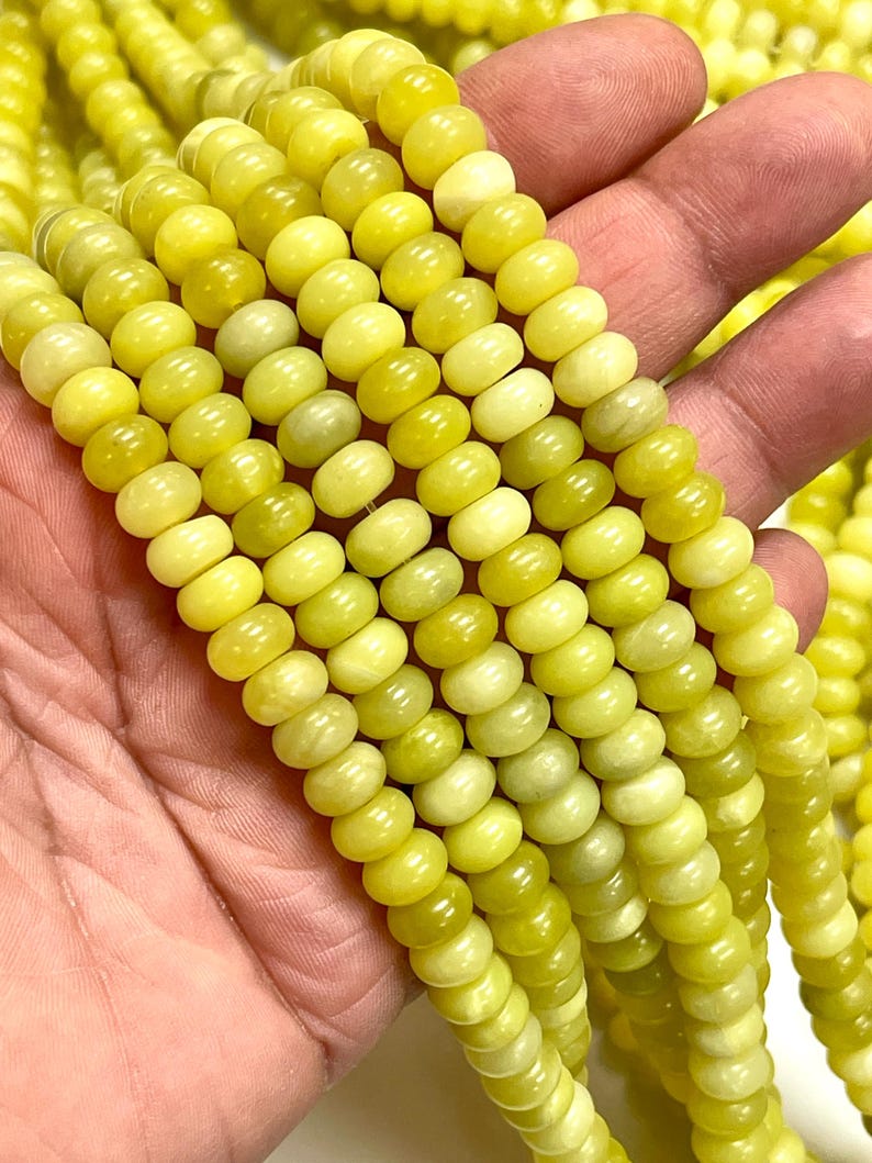 May include: Close-up of strands of yellow-green gemstone beads. The beads are small, round, and have a slightly irregular shape. The color varies from pale yellow to a deeper, olive-green hue. The beads are strung together, forming multiple strands.