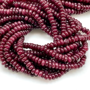 Puede incluir: Una hebra de cuentas de piedras preciosas de color rojo intenso, cada cuenta tiene una forma ovalada redondeada y una superficie ligeramente texturizada.