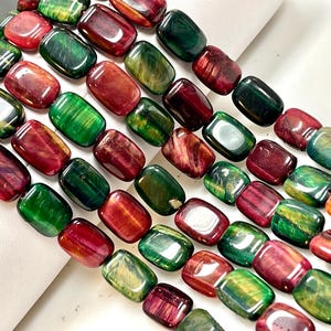 Op de afbeelding: Close-up van rechthoekige kralen in rood, groen en geel. De kralen zijn gepolijst en aan elkaar geregen, waarschijnlijk voor het maken van sieraden. Elke kraal is ongeveer 1,5 cm lang.