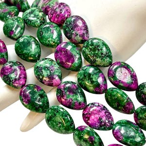 May include: Close-up of a strand of gemstone beads. The beads are oval-shaped, with a mix of deep green and vibrant magenta colors. The beads are strung together, showcasing their polished surfaces.