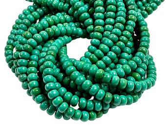 May include: A strand of turquoise green beads, each bead is round and slightly elongated. The beads are arranged in a circular pattern, creating a visual effect of a woven rope.