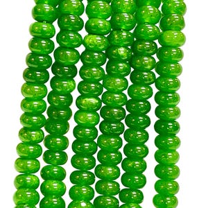 May include: Close-up of several strands of bright green beads. The beads are round and have a glossy finish. The beads are strung together, creating a textured pattern. The background is plain white.