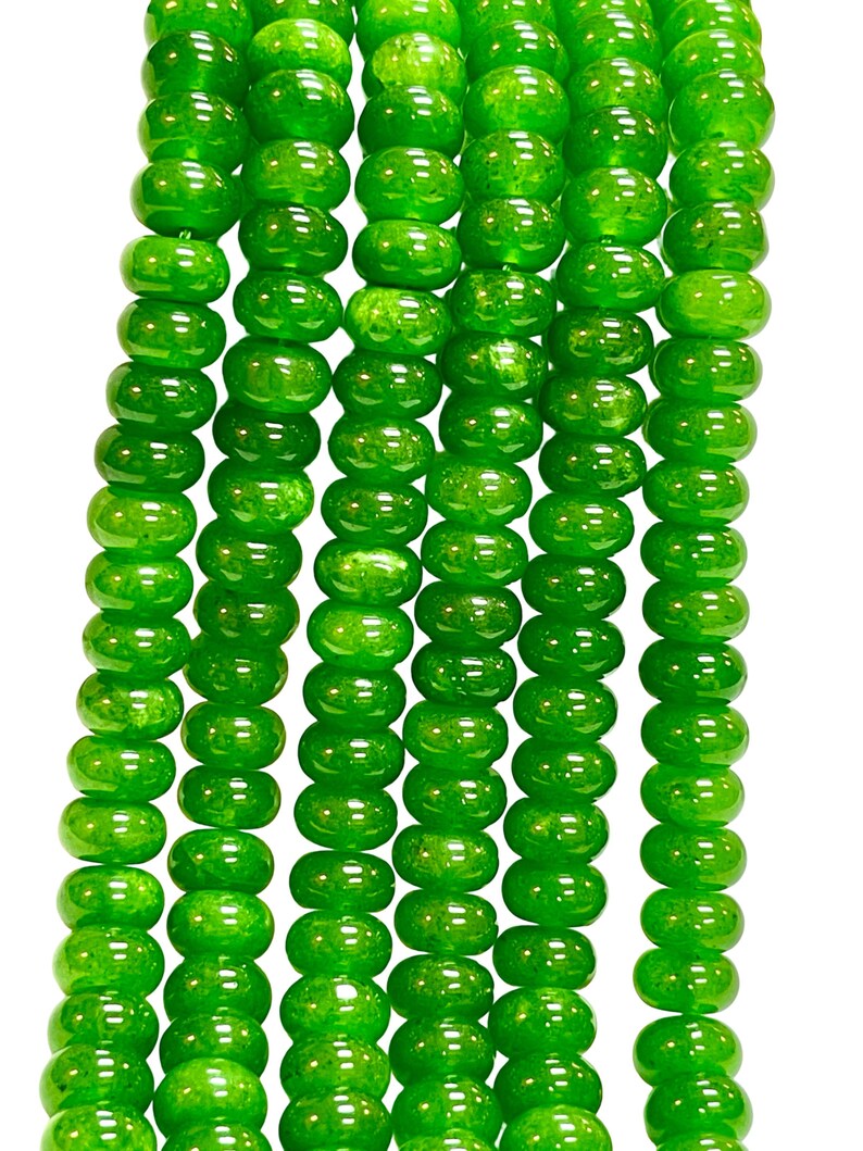 May include: Close-up of several strands of bright green beads. The beads are round and have a glossy finish. The beads are strung together, creating a textured pattern. The background is plain white.