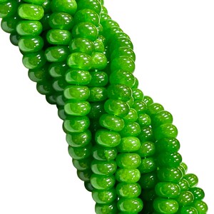 May include: Close-up of a strand of bright green beads. The beads are round and have a glossy finish, reflecting light. The beads are strung together, forming a flowing, curved pattern against a white background. The beads are a vibrant, eye-catching green.