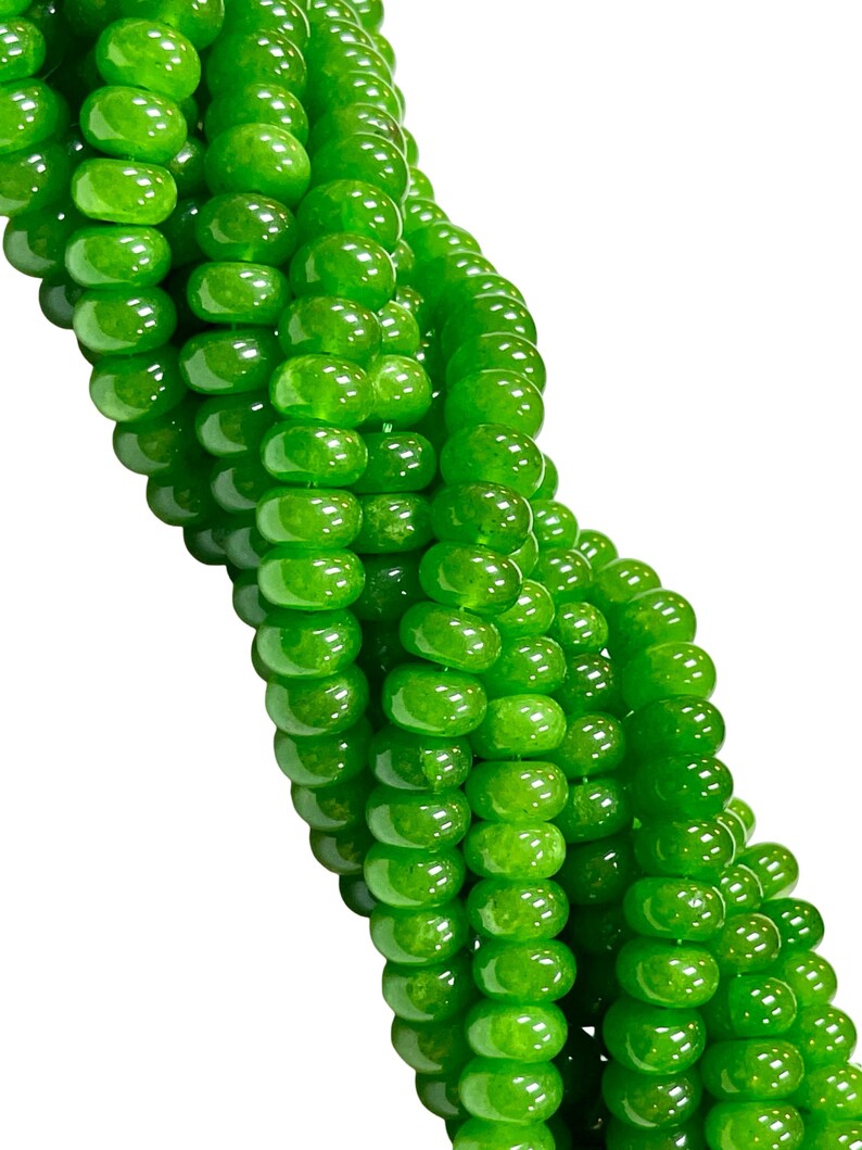 May include: Close-up of a strand of bright green beads. The beads are round and have a glossy finish, reflecting light. The beads are strung together, forming a flowing, curved pattern against a white background. The beads are a vibrant, eye-catching green.