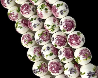 May include: White round beads with a floral pattern of pink roses and purple flowers. The beads are arranged in a vertical line.