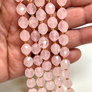 K&ouml;nnte beinhalten: Str&auml;nge aus facettierten, hellrosa Rosenquarzperlen. Die Perlen sind mit goldfarbenen Abstandshaltern und rosa Faden aufgef&auml;delt. Die Perlen haben ein geometrisches, facettenreiches Design.