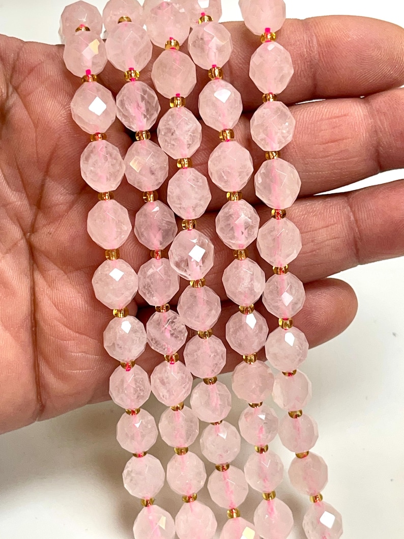 K&ouml;nnte beinhalten: Str&auml;nge aus facettierten, hellrosa Rosenquarzperlen. Die Perlen sind mit goldfarbenen Abstandshaltern und rosa Faden aufgef&auml;delt. Die Perlen haben ein geometrisches, facettenreiches Design.