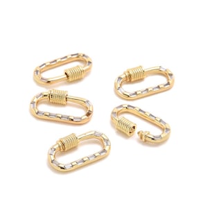 Puede incluir: Cinco cierres ovalados dorados con cierres de rosca. Cada cierre está adornado con pequeñas piedras rectangulares y transparentes. Los cierres se muestran sobre un fondo blanco.