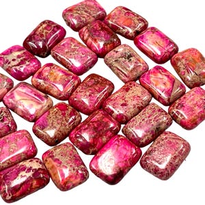 May include: A collection of rectangular, polished gemstones in shades of pink, red, and brown. The stones have a mottled appearance with varying patterns and textures. These gemstones are ideal for jewelry making or crafting.