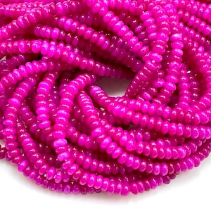 Puede incluir: Una hebra de cuentas de color rosa brillante, redondas y ligeramente alargadas. Las cuentas están hechas de un material liso y pulido y tienen un ligero brillo.