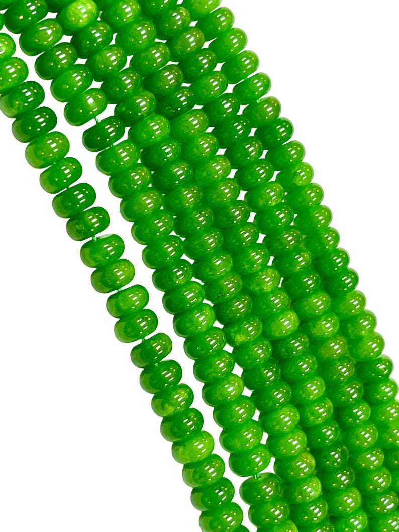May include: Close-up of several strands of bright green beads. The beads are round with a slightly flattened shape and a glossy finish. The beads are strung together, creating a flowing, textured appearance. The background is plain white.