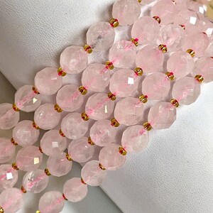 K&ouml;nnte beinhalten: Nahaufnahme von mehreren Str&auml;ngen facettierter, hellrosa Rosenquarzperlen. Die Perlen sind mit goldfarbenen Akzenten aufgef&auml;delt. Die Perlen sind oval und haben eine durchscheinende Qualit&auml;t.