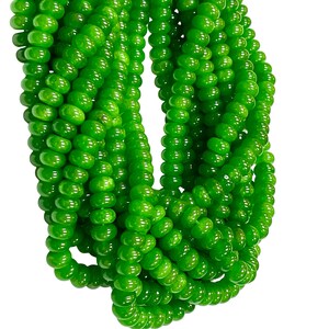 May include: Multiple strands of vibrant green beads. The beads are small, round, and uniform in size, creating multiple strands. The beads have a smooth, polished surface, reflecting light. The background is plain white.