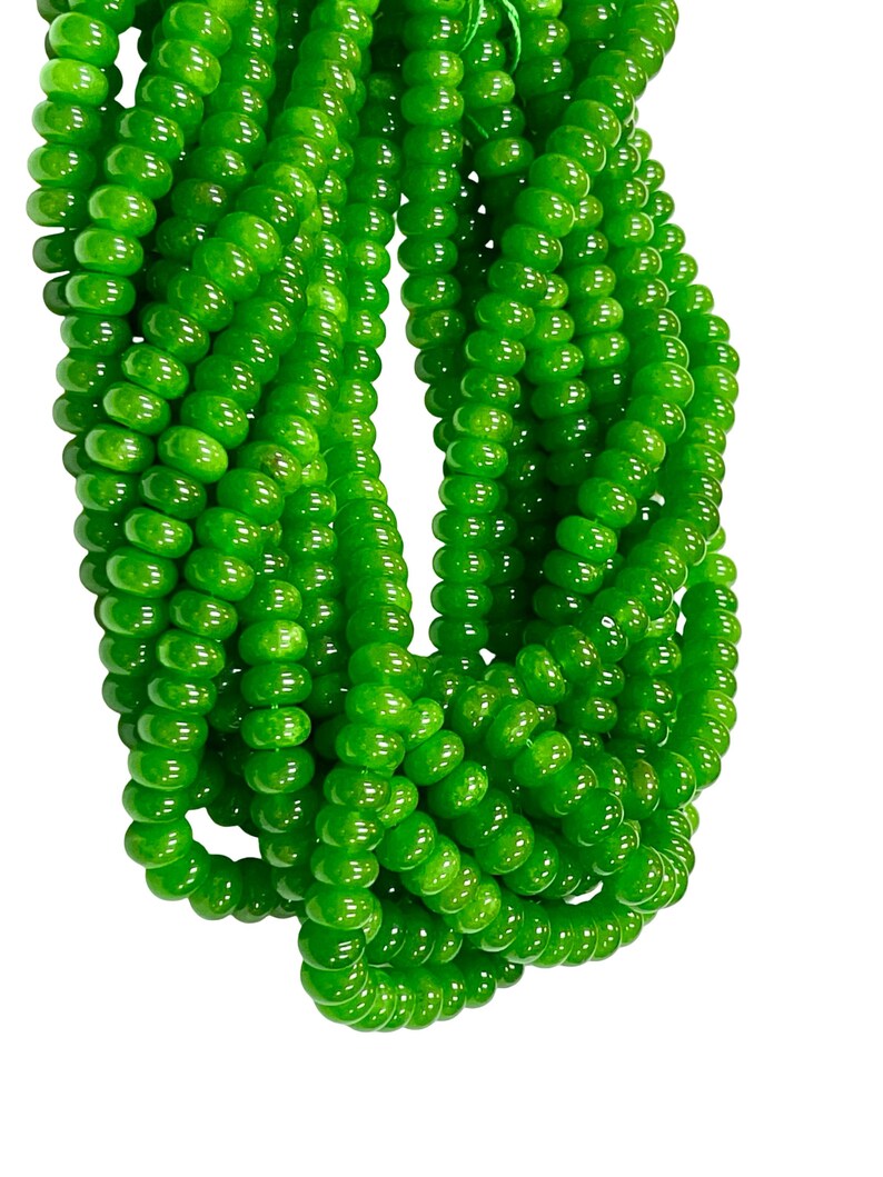 May include: Multiple strands of vibrant green beads. The beads are small, round, and uniform in size, creating multiple strands. The beads have a smooth, polished surface, reflecting light. The background is plain white.