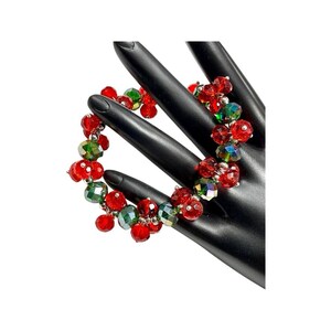 May include: A red and green beaded bracelet with iridescent crystals. The bracelet is made of small, faceted beads that are strung together on a silver wire.