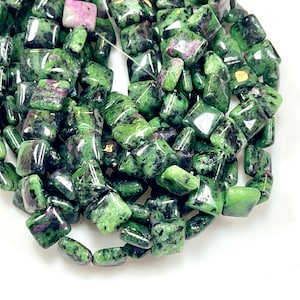 May include: A collection of green and black ruby zoisite beads. The beads are a mix of square and rounded shapes, with a polished, glossy finish. Some beads have patches of pinkish-red ruby.