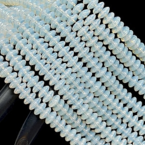May include: Close-up of multiple strands of opalescent, light blue beads. The beads have a unique, symmetrical shape with a central oval and radiating edges, strung together to form a necklace or bracelet.