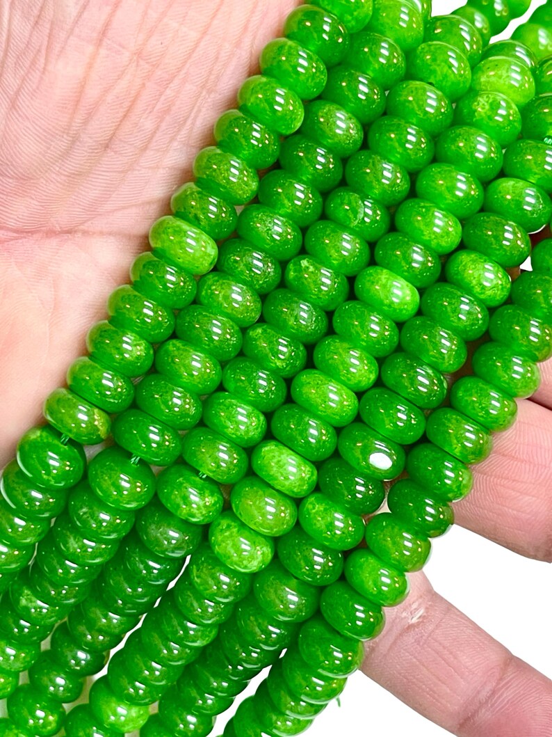 May include: Close-up of strands of bright green beads. The beads are round and have a glossy finish. The beads are strung together, creating a necklace or bracelet.