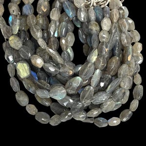 May include: A multi-strand necklace featuring faceted labradorite beads in shades of gray, blue, and green. The beads are oval-shaped and strung together, creating a layered effect. The necklace has a silver clasp and is set against a black background.