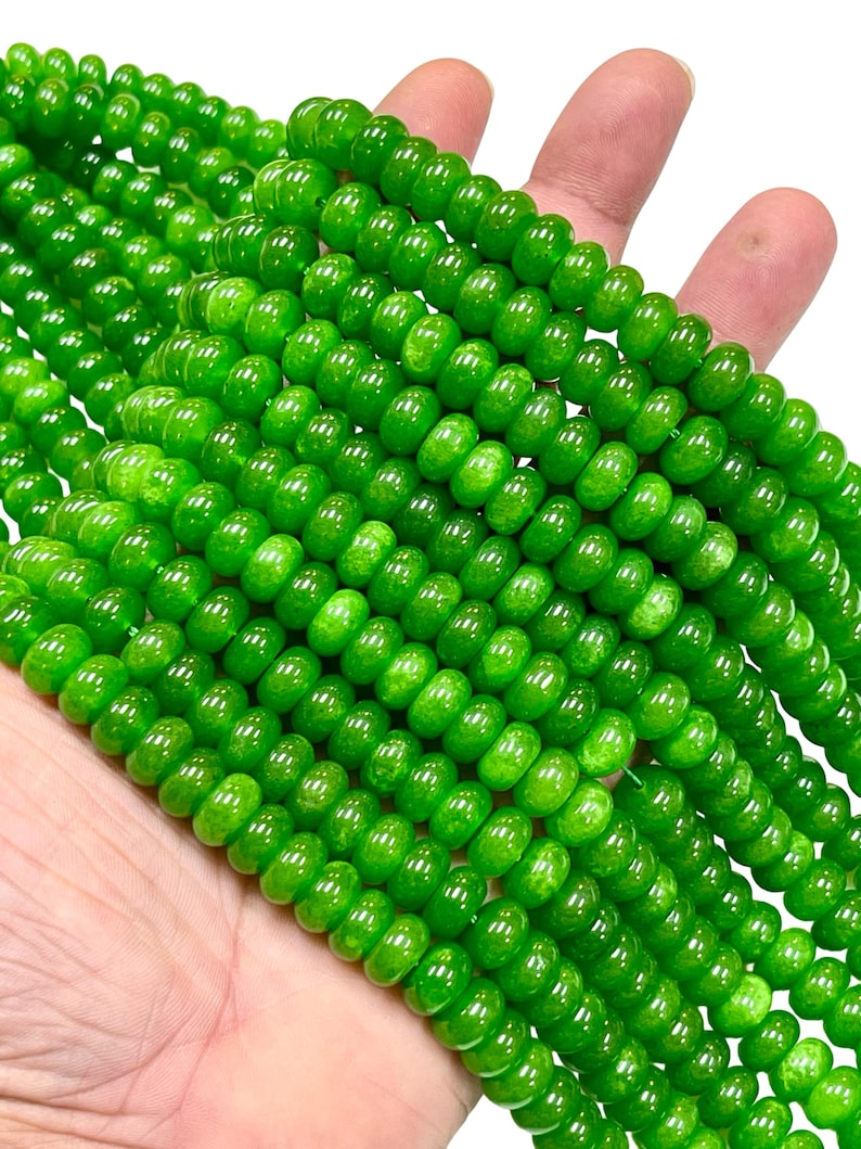 May include: Close-up of strands of bright green beads. The beads are round and have a glossy finish. The beads are held in a hand against a white background. The beads are a vibrant, eye-catching green.