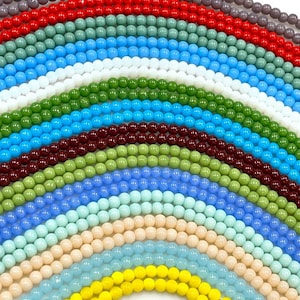 May include: Assortment of 18 strands of round glass beads in various colours, including red, green, blue, yellow, and white. The beads are arranged in a rainbow pattern.