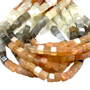 May include: A strand of square-shaped sunstone beads in shades of brown, gray, and white. The beads are arranged in a gradient pattern, with the darkest brown beads at one end and the lightest white beads at the other end.