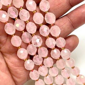 K&ouml;nnte beinhalten: Nahaufnahme von Str&auml;ngen facettierter, hellrosa Rosenquarzperlen. Die Perlen sind mit goldfarbenen Abstandshaltern aufgef&auml;delt. Die Perlen werden in einer Hand gehalten, was die zarte Farbe und Textur der Edelsteine zeigt.