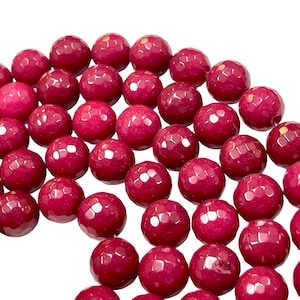 May include: A collection of faceted, round beads in a deep magenta hue. The beads have a textured surface and are arranged in a curved pattern against a white background. These beads are suitable for jewelry making.