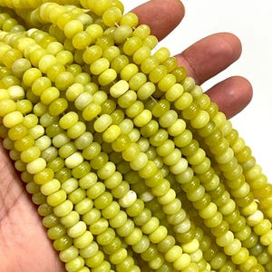 May include: Strands of yellow-green gemstone beads. The beads are small, round, and have a slightly flattened shape. The color varies from a pale yellow to a deeper, olive-green hue. The beads are strung together, creating a flowing, textured appearance.
