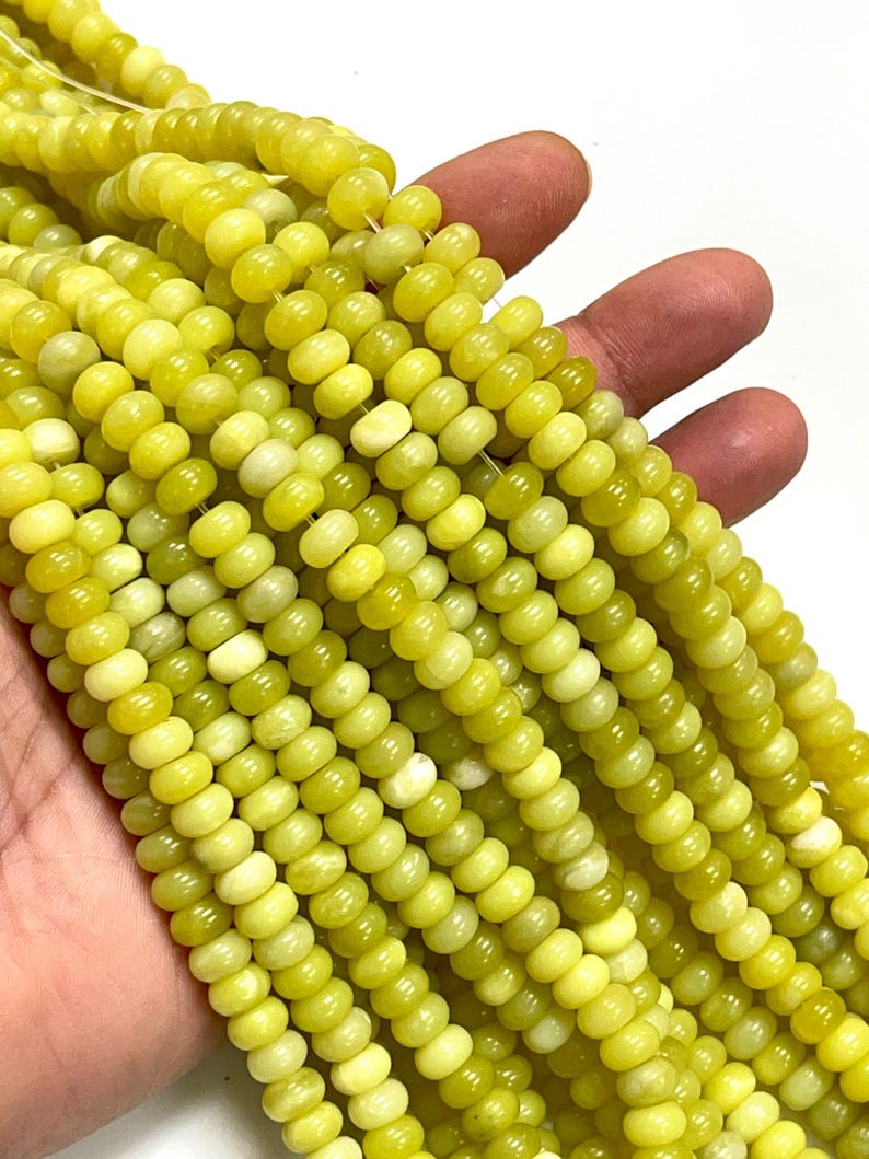 May include: Strands of yellow-green gemstone beads. The beads are small, round, and have a slightly flattened shape. The color varies from a pale yellow to a deeper, olive-green hue. The beads are strung together, creating a flowing, textured appearance.