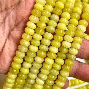 May include: Close-up of strands of yellow-green gemstone beads. The beads are round and have a slightly flattened shape. The color varies from a pale yellow to a deeper, more saturated green-yellow. The beads are strung together, ready for jewelry making.