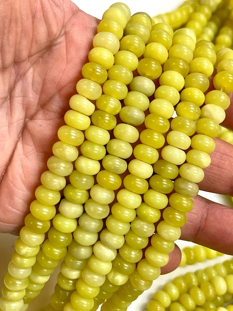 May include: Close-up of strands of yellow-green gemstone beads. The beads are round and have a slightly flattened shape. The color varies from a pale yellow to a deeper, more saturated green-yellow. The beads are strung together, ready for jewelry making.