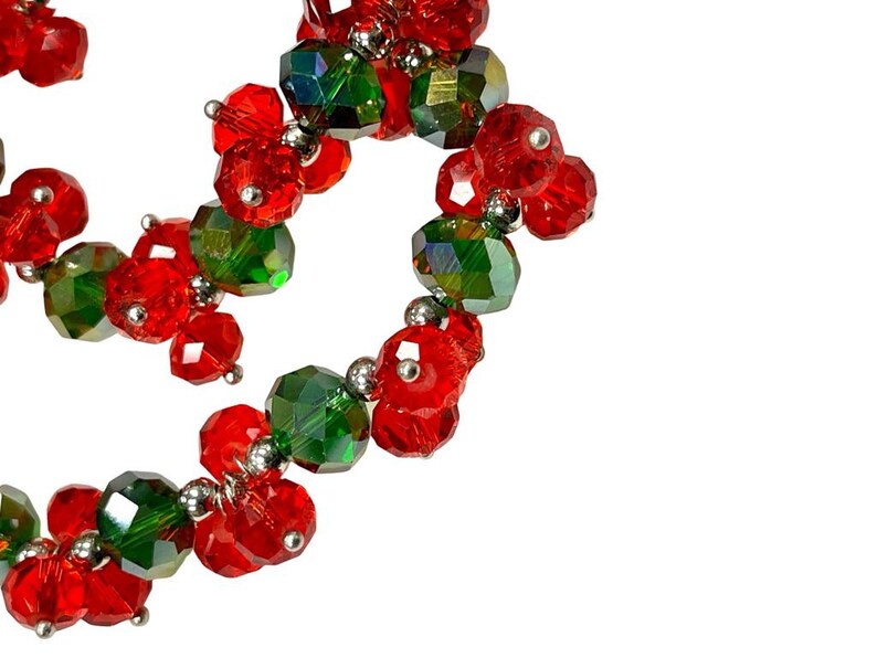 May include: A strand of red and green glass beads, strung together with silver metal connectors. The beads are arranged in a swirling pattern.