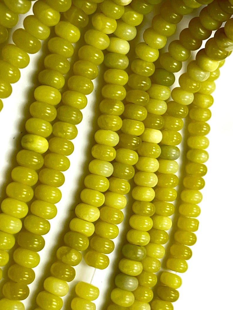 May include: Close-up of strands of olive-green gemstone beads. The beads are oval-shaped and strung together, creating a textured surface. The beads have a glossy finish and vary slightly in color, ranging from light to dark olive green.