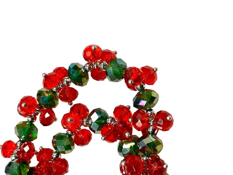 May include: A close-up of a red and green beaded garland. The beads are made of glass and have a shiny finish. The garland is strung on a silver wire.