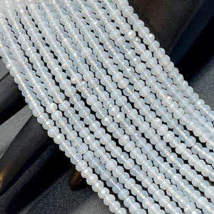 May include: Strands of light blue, faceted beads. The beads are small and uniform in size, strung together to create a delicate and shimmering effect. The beads are displayed against a dark background.