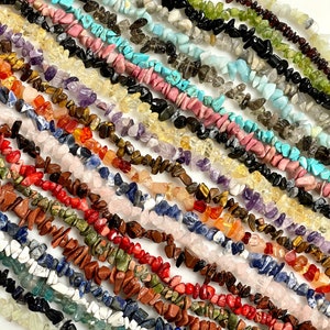 May include: Assortment of chip beads in various colors and textures, including turquoise, amethyst, rose quartz, tiger's eye, and red jasper. The beads are arranged in rows, showcasing their unique shapes and patterns.