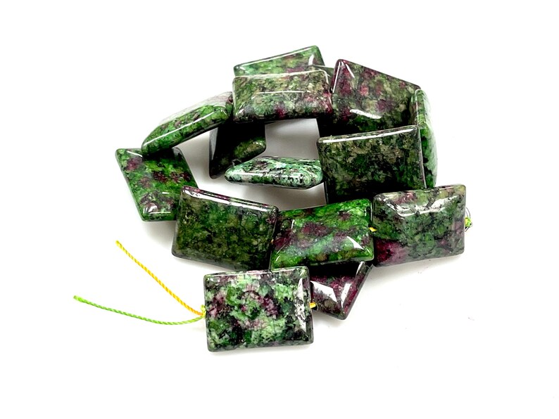 Puede incluir: Un conjunto de cuentas rectangulares de rub&iacute; zoisita. Las cuentas son una mezcla de colores verde y burdeos, con un acabado pulido y brillante. Las cuentas est&aacute;n ensartadas con hilo amarillo y verde.