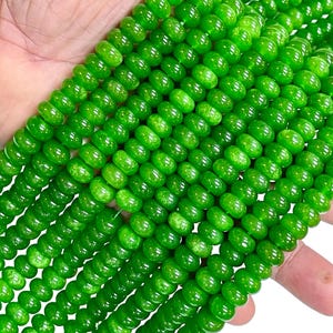 May include: Close-up of strands of bright green beads. The beads are round and have a glossy finish. The beads are strung together, creating a textured and visually appealing pattern. The beads are a vibrant green colour.