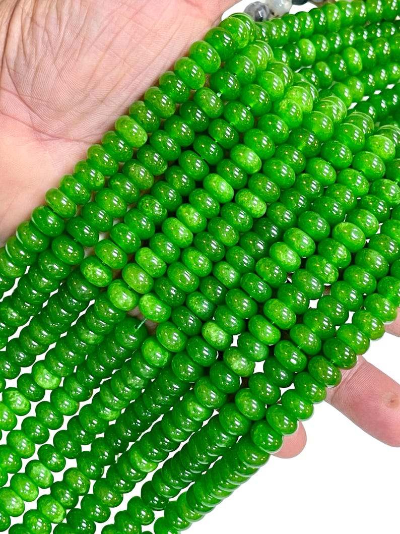 May include: Close-up of strands of bright green beads. The beads are round and have a glossy finish. The beads are strung together, creating a textured and visually appealing pattern. The beads are a vibrant green colour.