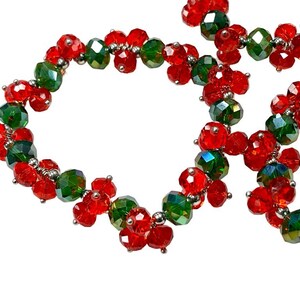 May include: A red and green beaded necklace with alternating crystal beads. The necklace is made of small, faceted beads that are strung together on a silver wire.
