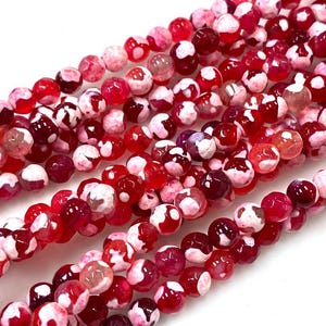 May include: A strand of red and white agate beads. The beads are round and have a mottled appearance.
