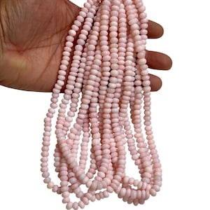 May include: Strands of light pink, round beads. The beads are strung together, forming multiple necklaces or strands. The beads have a smooth, polished appearance and are a consistent size. The background is plain white.