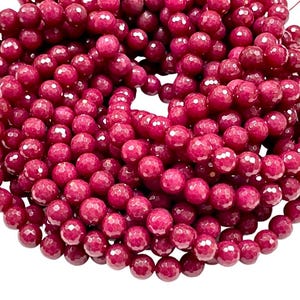 May include: A strand of deep red faceted gemstone beads. The beads are round and have a smooth, polished finish.