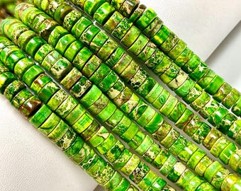 Può includere: Primo piano di fili di perline di diaspro verde. Le perline sono cilindriche con un mix di tonalità verdi chiare e scure, e alcune hanno accenti gialli e marroni. Le perline sono disposte in file parallele.