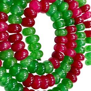 May include: Close-up of a necklace featuring alternating strands of vibrant green and deep red beads. The beads are smooth and rounded, creating a visually appealing pattern. The necklace is likely made of gemstones or glass.