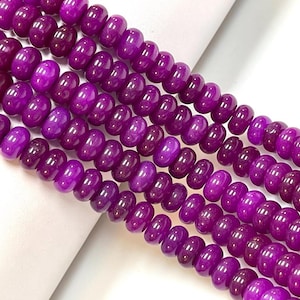 May include: Strands of polished, deep purple beads. The beads are barrel-shaped and strung together, creating a rich, textured appearance. The color varies slightly, adding depth to the design. Ideal for jewelry making.